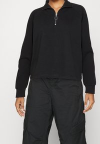 Svart sweatshirt med halvdragkedja, raglanärmar och ribbade muddarmar. Tillverkad av mjukt tyg med en avslappnad passform.