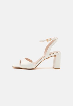 White faux leather high-heel sandal with a block heel, open toe, adjustable ankle strap, and subtle shiny texture.