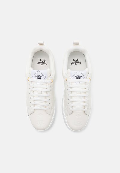 Zapatillas blancas con una parte superior sintética lisa, que presentan una lengüeta texturizada, cordones blancos, detalle del logo en relieve y un pequeño acento naranja.