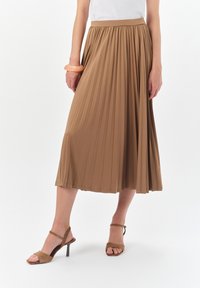Plisowana spódnica do kolan w jasnobrązowej tkaninie o gładkiej teksturze. Połączona z brązowymi sandałami na obcasie i bransoletką w kolorze brzoskwiniowym.