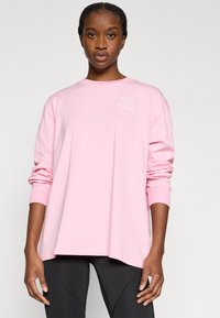 Jasnoróżowa, długorękawowa koszulka z miękkiej bawełny, o luźnym kroju z nadrukiem logo na piersi. Zaokrąglony dół i ściągacze na rękawach.