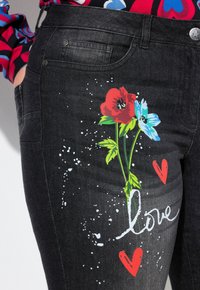 Jeans de mezclilla negra con un estampado floral de flores rojas y azules, acentuados con salpicaduras blancas y la palabra "amor" en cursiva.
