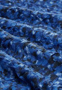 Blau gemusterter Stoff mit einer zerknitterten Textur, der dunkelblaue und schwarze abstrakte Formen auf einem hellblauen Hintergrund zeigt.