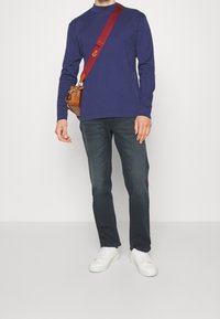 Marinblå långärmad skjorta, matchad med mörka jeans och vita sneakers. Brun axelväska med röd rem och metallhandtag.