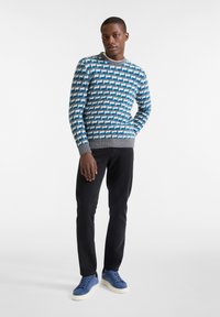 Suéter de punto con patrón geométrico en azul, gris y blanco, cuello redondo y puños acanalados; combinado con pantalones negros y zapatillas azules.