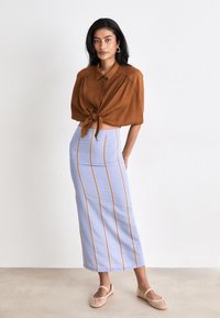 Bruine korte mouwen, knoop-shirt geknoopt in de taille; lichtblauwe, gestreepte midi-rok met verticale lijnen; huidkleurige gevlochten flats.