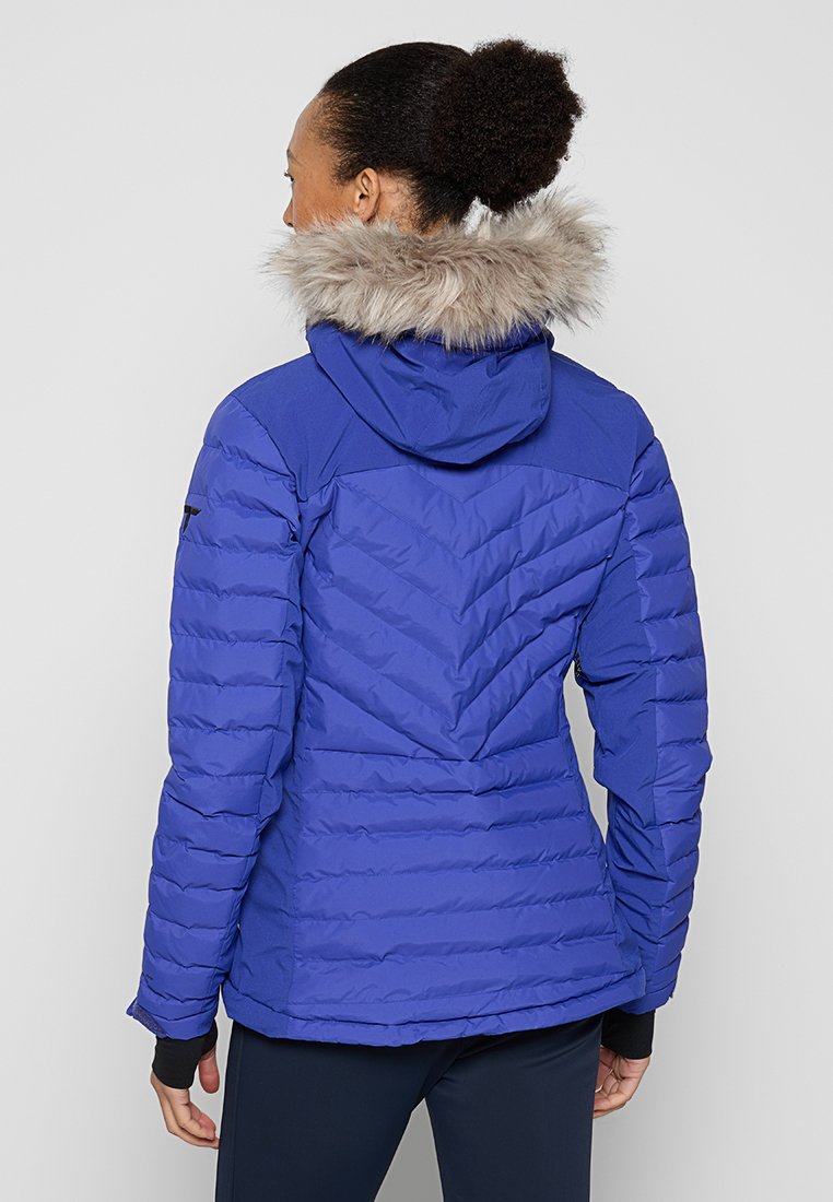 Veste bleue rembourrée avec un design matelassé, capuche ornée de fausse fourrure, et accent noir sur l'épaule, vue de dos.