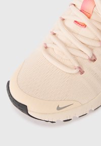 Scarpa sportiva di un beige chiaro con una tomaia in mesh testurizzato, dettagli rosa e suola in gomma nera. Logo swoosh ben visibile sul lato.