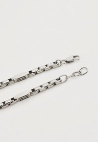 Ασημένια μεταλλική αλυσίδα με αλληλοσυνδεόμενους κρίκους, με επίπεδο σχέδιο και κυλινδρικά τμήματα. Ο εξοπλισμός περιλαμβάνει κλειδώματα για σύσφιξη.