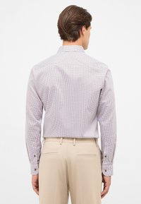 Wit overhemd met lange mouwen en een klein rood stippenpatroon. Voorzien van een spitse kraag en knopenmanchetten. G gedragen met beige broek.