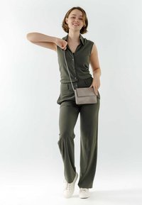 Oliven grøn ærmeløs jumpsuit med knaplukning og bæltestropper, parret med en lysegrå crossbody taske og hvide sneakers.