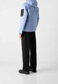 Puffjacka i ljusblått med horisontell söm, huva och en svart patch på vänster ärm. Svarta vida byxor och klumpiga svarta skor.