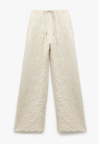 Weite Hosen aus strukturiertem, hellbeigem Stoff. Mit einer Kordelzug- Taille mit goldenen Akzenten und filigranen Faltenmustern durchgehend.