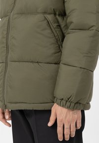 Pikowana kurtka puchowa w oliwkowym kolorze z zamkiem błyskawicznym, pikowanym wzorem, elastycznymi mankietami i gładką, błyszczącą fakturą.