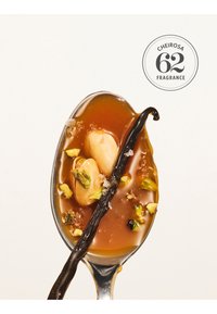 Łyżka z sosem karmelowym, dwie orzechy, zielone kawałki pistacji, strąk wanilii i płatki soli na jednolitym tle.