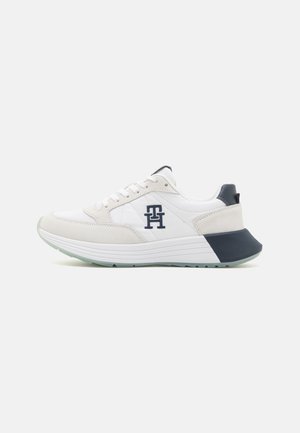 Low-profile white sneaker with suede accents, navy heel counter, thick white sole, and navy "TH" logo on side.