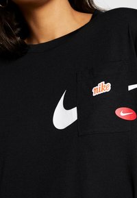 Czarny bawełniany t-shirt z wyra�źnym białym swooshem Nike oraz kieszenią z czerwonym i pomarańczowym logo Nike.