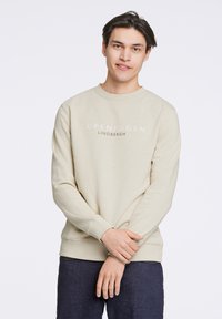Felpa beige chiaro con collo rotondo e maniche lunghe, con "COPENHAGEN LINDBERGH" stampato in un testo più scuro sulla parte anteriore.