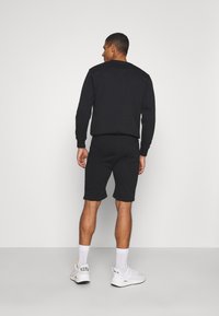 Black sweatshirt and black shorts combined outfit, featuring a fitted design. The model wears white sneakers with contrasting accents.