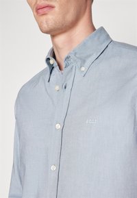 Ljusblå knapp-up skjorta i bomull med en fin textur. Har en liten broderad logotyp "BOSS" och vita knappar.