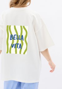 Overmaat katoenen t-shirt in off-white met een grafische print van groene golvende lijnen en "BELLA VITA" in het blauw op de achterkant.