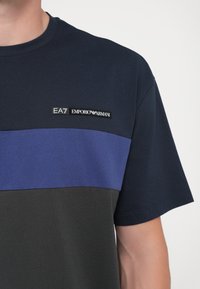 EA7 Emporio Armani T-skjorte i bomull, med marineblå, lilla og mørkegrå fargeblokker, og en logotag på brystet i svart.