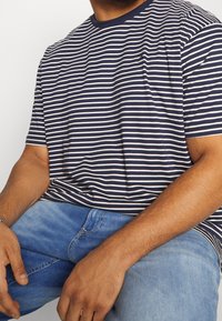 Marinblå och vit randig t-shirt i bomull med rund halsringning och korta ärmar, tillsammans med ljusblå denimjeans.