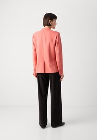 Korallblazer med skräddarsydd design, enkel ryggslits och knäppta ärmslut, kombinerad med svarta vida byxor.