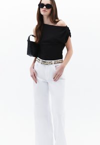 Top nero senza spalline, pantaloni bianchi a gamba larga, cintura con motivo, borsa a tracolla nera intrecciata e occhiali da sole neri. Design minimalista, texture liscia.