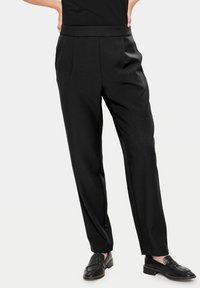 Pantalon noir ajusté avec une texture lisse, doté d'une taille haute, d'un devant plissé et de jambes fuselées. Associé à des mocassins noirs.