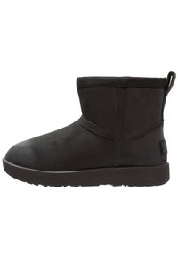 Czarny zamszowy botek z zaokrąglonym noskiem, niską cholewką, płaską gumową podeszwą i minimalistycznymi przeszyciami. Posiada pętelkę z tyłu do łatwego zakładania.