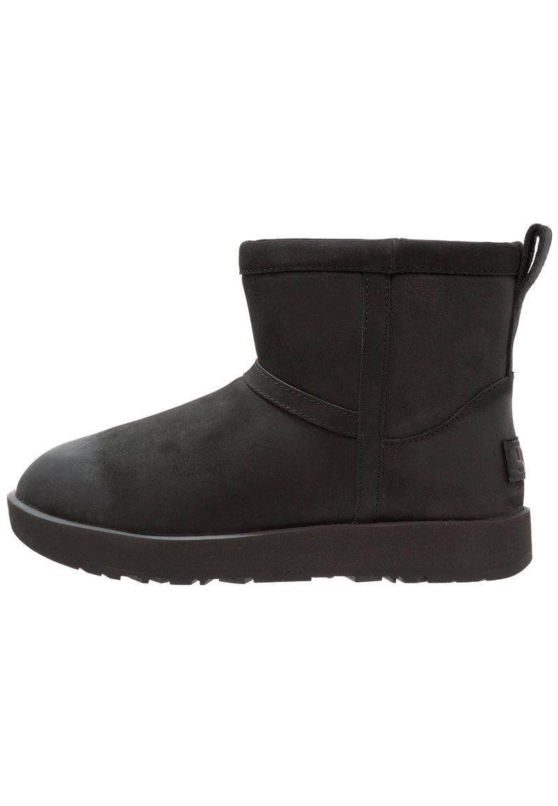 Czarny zamszowy botek z zaokrąglonym noskiem, niską cholewką, płaską gumową podeszwą i minimalistycznymi przeszyciami. Posiada pętelkę z tyłu do łatwego zakładania.