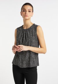 Bluză neagră fără mâneci cu un decolteu strâns, având un model alb cu puncte și o croială lejeră, asortată cu pantaloni negri.