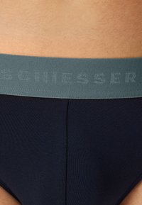 Marineblaue Unterwäsche mit einem weichen, elastischen grauen Bund, der das Wort "SCHIESSER" in subtiler, erhabener Textur zeigt.