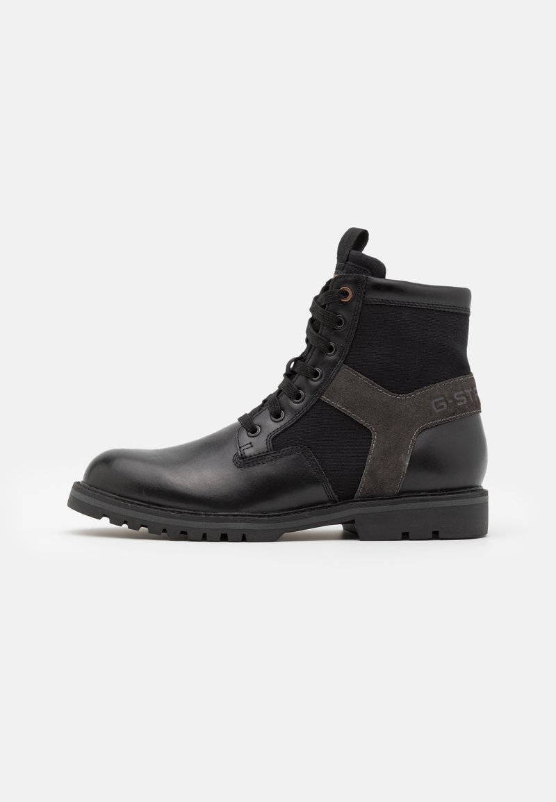 Stivaletto alla caviglia in pelle nera e tessuto con lacci, suola robusta e dettaglio incrociato in camoscio sul lato, su sfondo bianco.