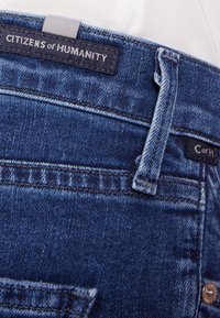 Tmavě modré džíny z denimu s hladkým povrchem. Mezi vlastnosti patří vybledlý vzhled, kontrastní šití a kožená štítková značka na pásu.