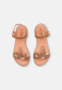 Ruske sandale s pletenim trakama, koja imaju kopčanje na automatsku kopču, glatku teksturu i bež tkaninu kao naglasak na gornjem delu. Ravni đon sa otisnutim logom unutra.