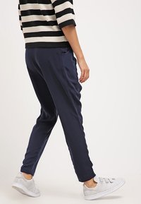 Granatowe, zwężane joggery z gładkiego materiału, z bocznymi kieszeniami. Połączone z jasnoszarymi sneakersami, stylizowane z czarno-białą paskowaną bluzką.