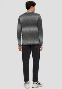 Szary sweter w paski o prążkowanej teksturze, z okrągłym dekoltem i kontrastującymi jasnymi oraz ciemnymi odcieniami. Noszony z czarnymi dżinsami i trampkami.