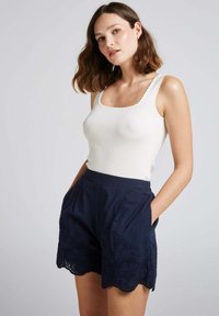 Débardeur blanc côtelé avec des bords scallopés associé à un short bleu marine avec broderie florale et un ourlet scallopé, poches plates à l'avant.
