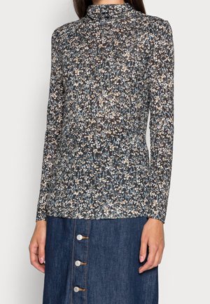 Kobieta ubrana w dopasowany golf z długim rękawem w kwiatowy wzór, zestawiony z ciemnoniebieską spódnicą dżinsową zapinaną na guziki z przodu.