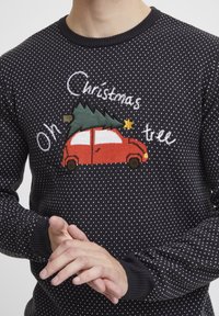 Maglione nero a maglia con pois bianchi, caratterizzato da un'auto rossa ricamata con un albero di Natale, e la scritta "Oh albero di Natale."