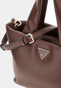 Braune Lederhandtasche mit einem lässigen Design, goldfarbenen Details, verstellbarem Trageriemen und einer dreieckigen Logo-Plakette.