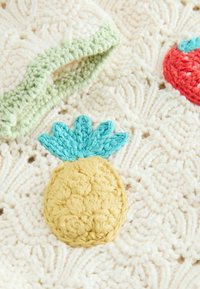 Tejido de punto en color crema con un motivo texturizado de piña en amarillo y turquesa, con un borde de acento verde y patrones de bucles intrincados.