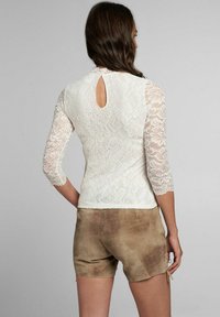 Weißes Spitzentop mit drei Viertel Ärmeln, das hinten mit einem Schlüsselloch-Ausschnitt versehen ist, kombiniert mit hellbraunen Wildleder-Shorts.