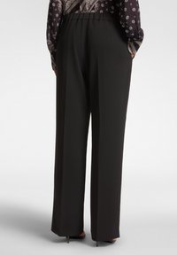 Czarne spodnie o szerokich nogawkach z gładką teksturą, elastycznym paskiem w talii oraz dwiema bocznymi kieszeniami. Zaprojektowane z myślą o luźnym, swobodnym kroju.
