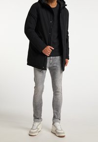 Sort isoleret jakke med hætte, der har lynlås og trykknaplukning, parret med grå jeans og hvide sneakers med grå detaljer.