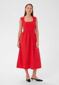 Punane kleit ruudu kaelusega, ribastatud bodiga, laiendatud seelik ning sile tekstuur, koos mustade kontsatoosidega.