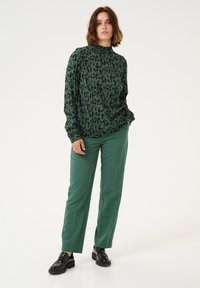 Top a maniche lunghe verde con motivo, con collo alto, abbinato a pantaloni verdi a gamba dritta e mocassini neri. Tessuto morbido e vestibilità comoda.