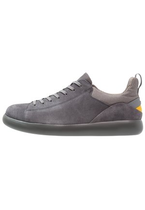 Niskoprofilowy szary sneaker z cholewką zamszową, siateczkowym kołnierzem, sznurowaniem z przodu, wyściełaną piętą i gumową podeszwą z żółtym detalem z tyłu.